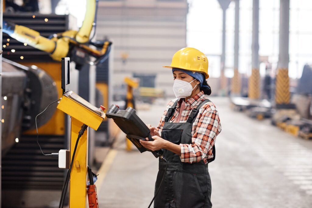 Young female technician using remote switch to control industrial machine
